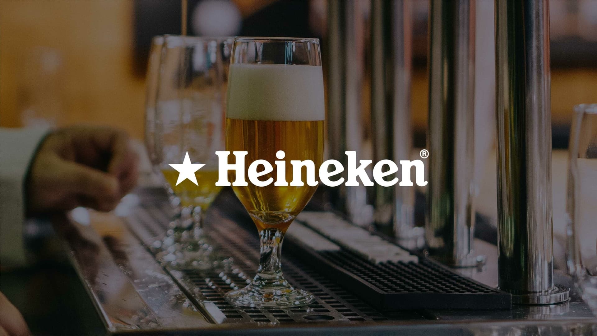 Heineken logo in white with a background of a bar dispensing freshly poured beer